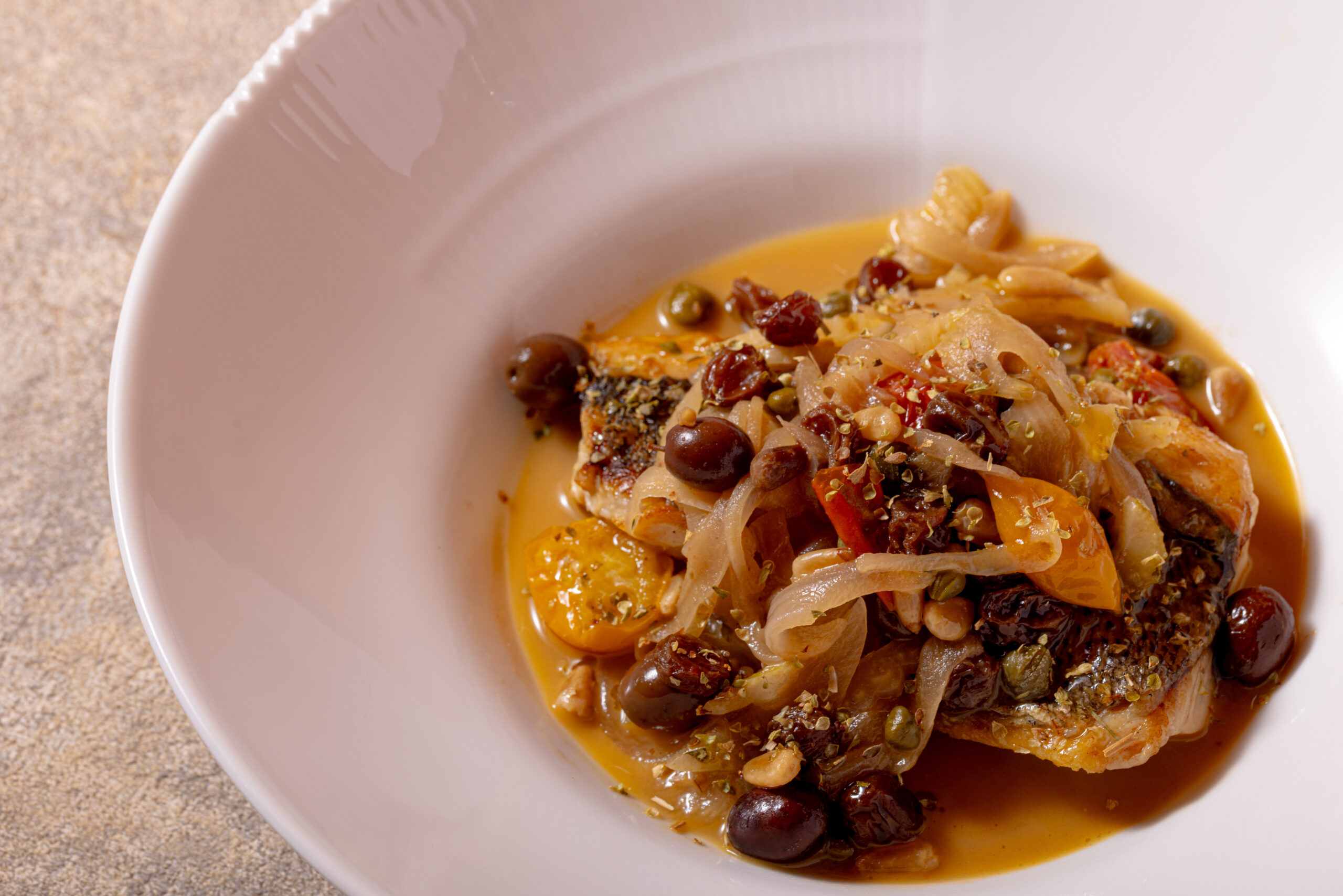 赤玉葱・セロリ・レーズン・松の実・ケッパー・オリーブ・アンチョビ・ミニトマトをその日仕入れた白身魚と煮込み、オレガノとミントで爽やかな香りを添えたシチリアの郷土料理「マタロッタ」